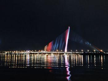 Illuminated bridge over river against sky at night