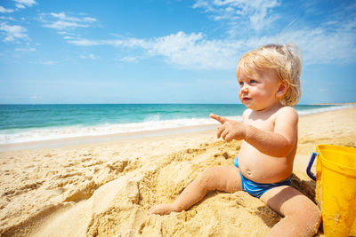 Portrait of boy sitting at beach against sky