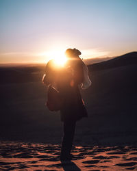 Full length side view of silhouette woman carrying son on sand dune during sunset