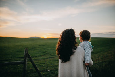 Rear view of mother carrying daughter while standing on landscape against sky