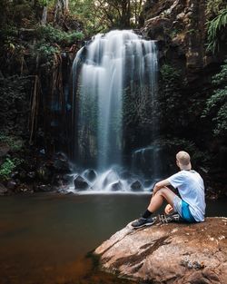 Man sitting on rock by waterfall in forest