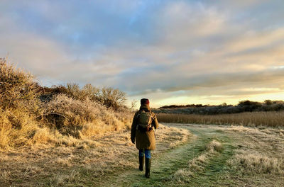 Rear view of woman waking on field against sky