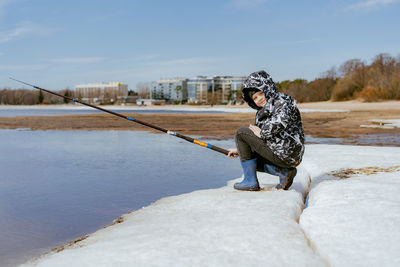 Cute little caucasian boy holding a fishing rod looking into distance on sea side on spring day