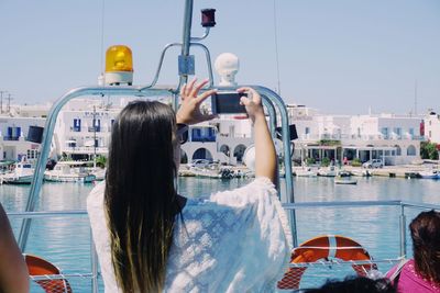 Rear view of woman photographing with smart phone on boat in city