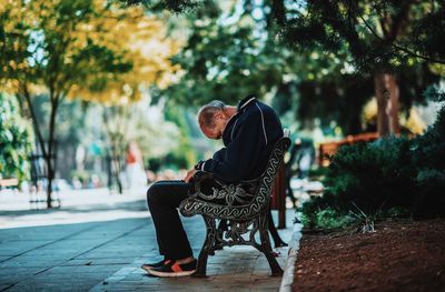 Side view of man sitting on seat in park