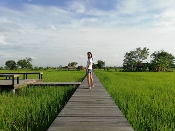 Rear view of woman on footpath amidst grass against sky