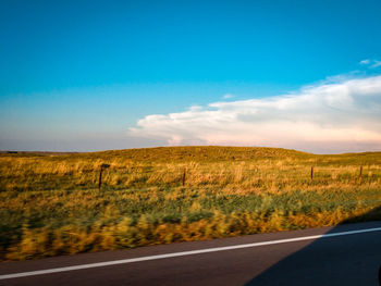 Road by field against blue sky