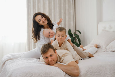 Family with two kids on the bed having fun. mather, father baby and toddler sons are happy in the