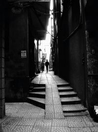 Rear view of man walking on footpath amidst buildings