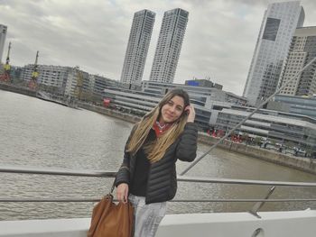 Portrait of woman standing against river in city