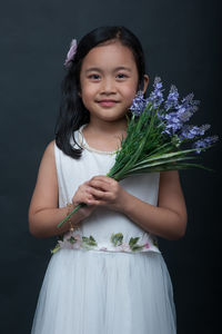 Portrait of smiling girl with flowers standing against black background