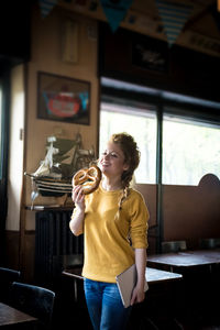 Smiling young woman holding pretzel and digital tablet in cafe