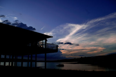 Silhouette building by lake against sky during sunset