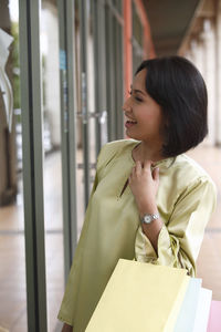 Woman holding shopping bags while standing in corridor