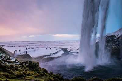 Scenic view of waterfall by snow covered landscape against cloudy sky during sunset