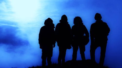 Silhouette of friends standing against blue sky