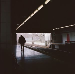 Rear view of silhouette man walking on illuminated railroad station