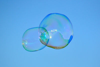 Low angle view of bubbles flying against clear blue sky