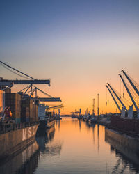 Cranes at harbor against clear sky during sunset