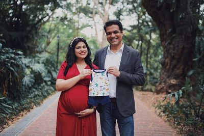 Portrait of couple holding baby clothing while standing outdoors