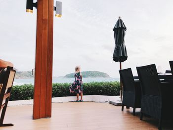 Rear view of woman standing on chair against sky