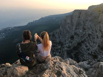 Rear view of women sitting on rock against mountains