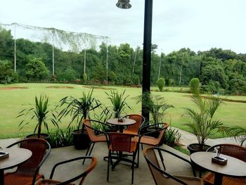 Empty chairs and tables by swimming pool against sky