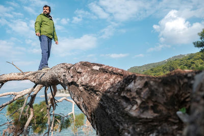 Frontal view of man standing on tree against sky