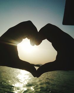 Close-up of silhouette hand holding heart shape against sky during sunset