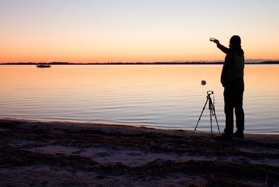 Silhouette man standing at beach against sky during sunset