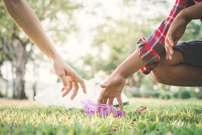 Cropped hands picking plastic water bottle from grassy field at public park