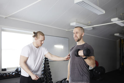 Man exercising with dumbbell with trainer checking his progress