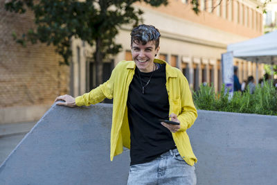 Portrait of a non binary person looking at camera while using mobile phone outdoors. person