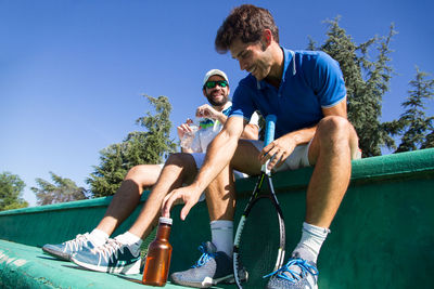 Tennis players sitting on steps against sky