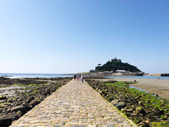 Footpath by sea against clear sky