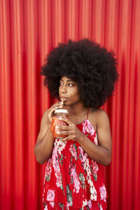 Woman drinking smoothie while standing in front of red wall