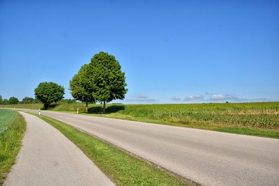 Road amidst field against clear blue sky