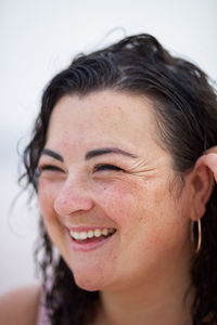 Smiling curvy female adjusting wet wavy hair and looking away on blurred background