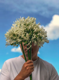 Midsection of man holding bouquet of white flowers against cloudy sky