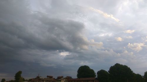 Low angle view of trees and building against storm clouds