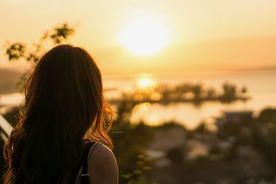 Rear view of young woman standing at beach against sky during sunset