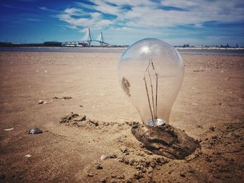 Abandoned light bulb in sand at beach against sky