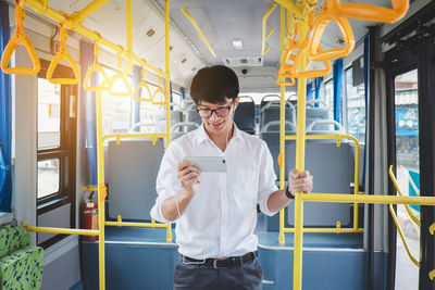 Smiling young man using mobile phone while standing in bus