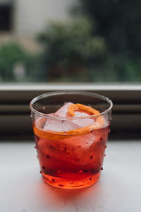 Electric red orange negroni cocktail in polka dot glass on window sill with lush green background