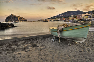 Boat moored on beach against sky during sunset