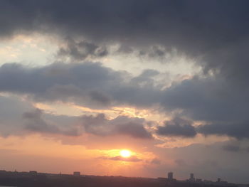 Low angle view of sunlight streaming through silhouette buildings against sky