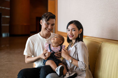 Asian muslim couple with one year old baby daughter, at long light brown sofa, long hair, portrait