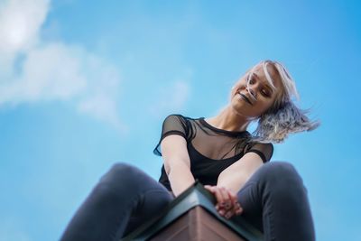 Low angle view of woman sitting against blue sky
