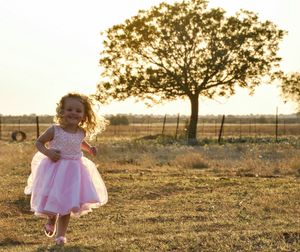 Portrait of happy girl in dress running on grassy field against clear sky