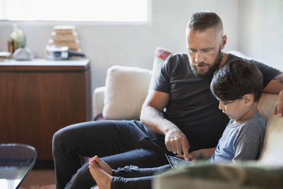 Father assisting son in using digital tablet on sofa at home